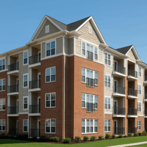 Four-story apartment building with red brick and beige siding in a suburban Southern Wisconsin neighborhood.